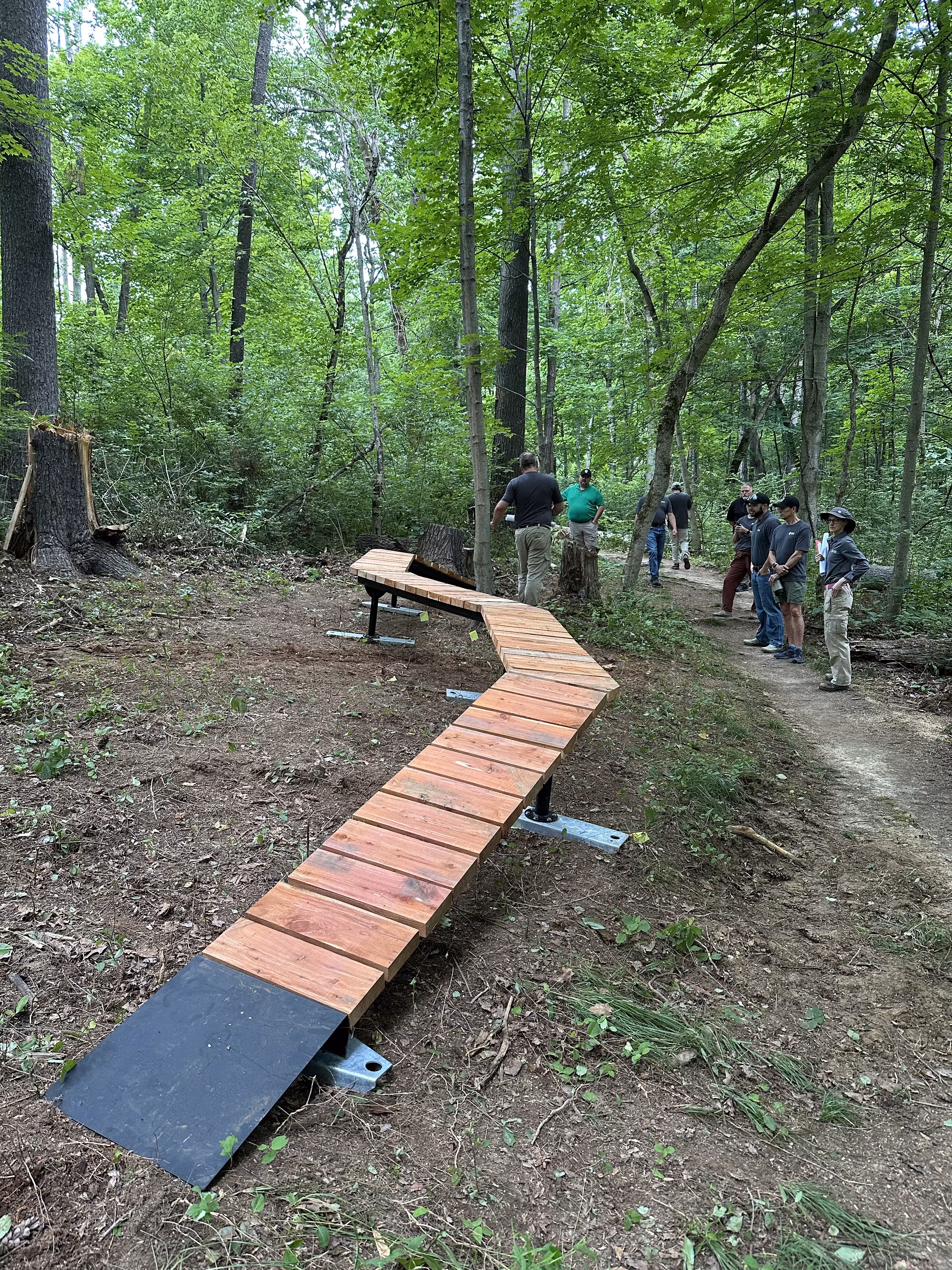 a group of people standing around a wooden mountain bike path in the woods