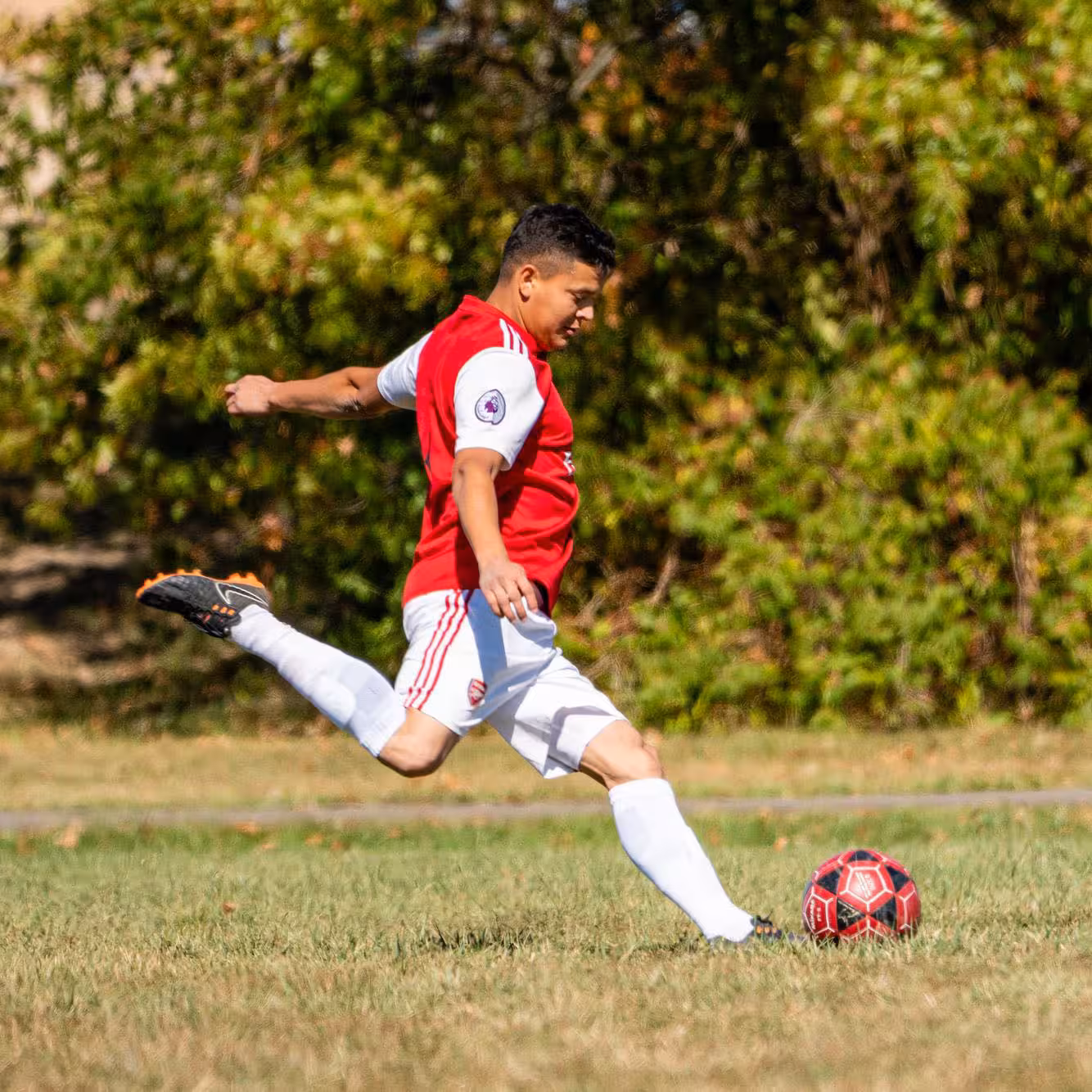 Man in red jersey kicking a soccer ball at Francis Recreacres