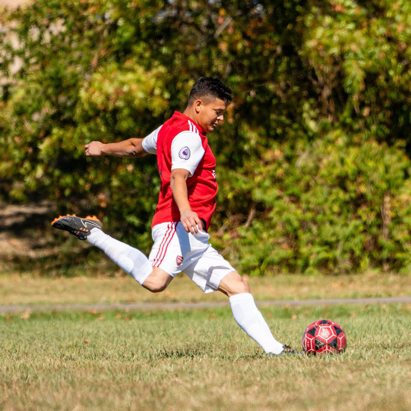 Man in red jersey kicking a soccer ball at Francis Recreacres
