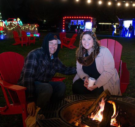 a man and woman sitting in chairs around a fire pit