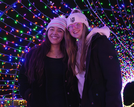 two women standing in front of a string of lights